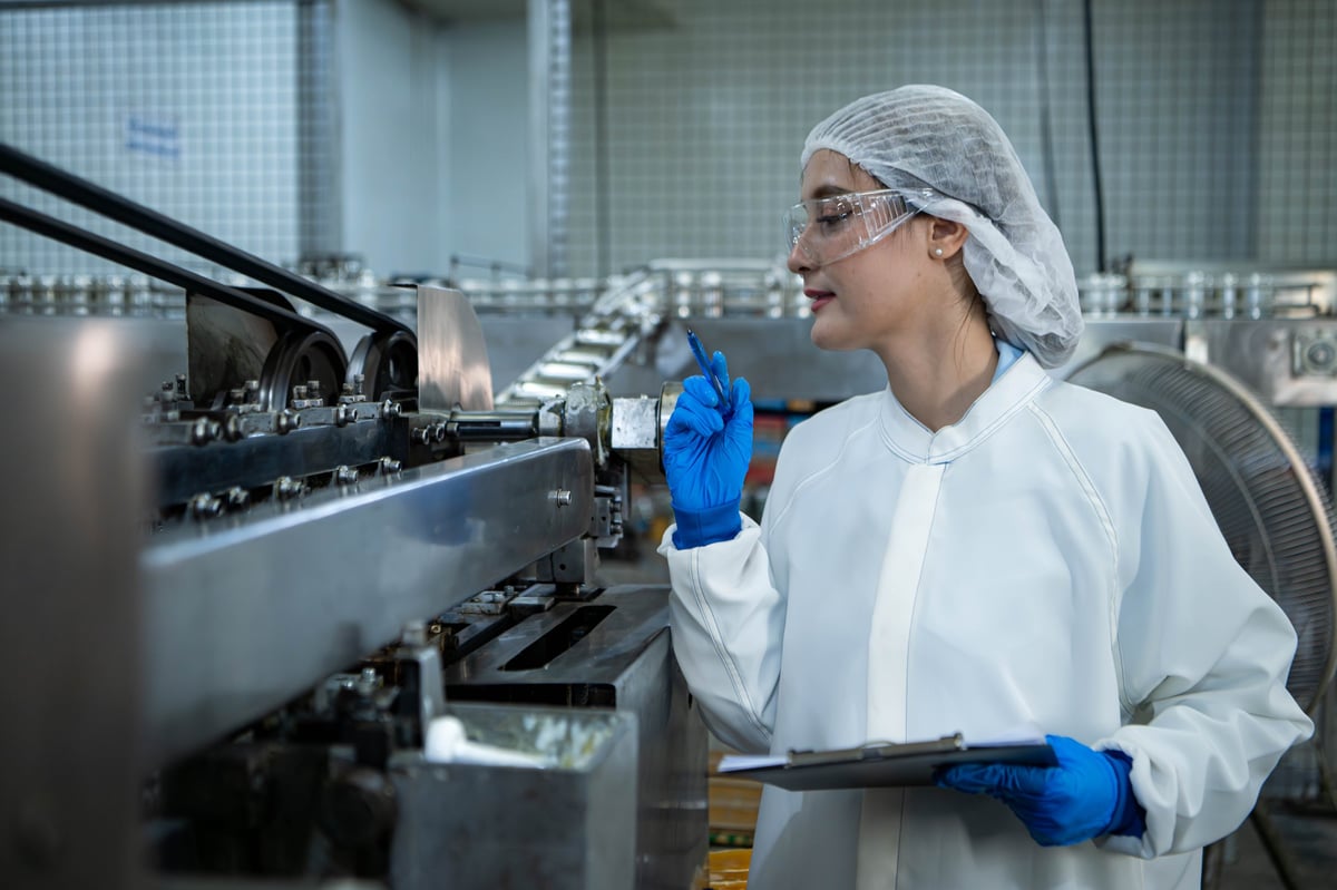 Food scientist inspecting a canned fish production line and recording quality data