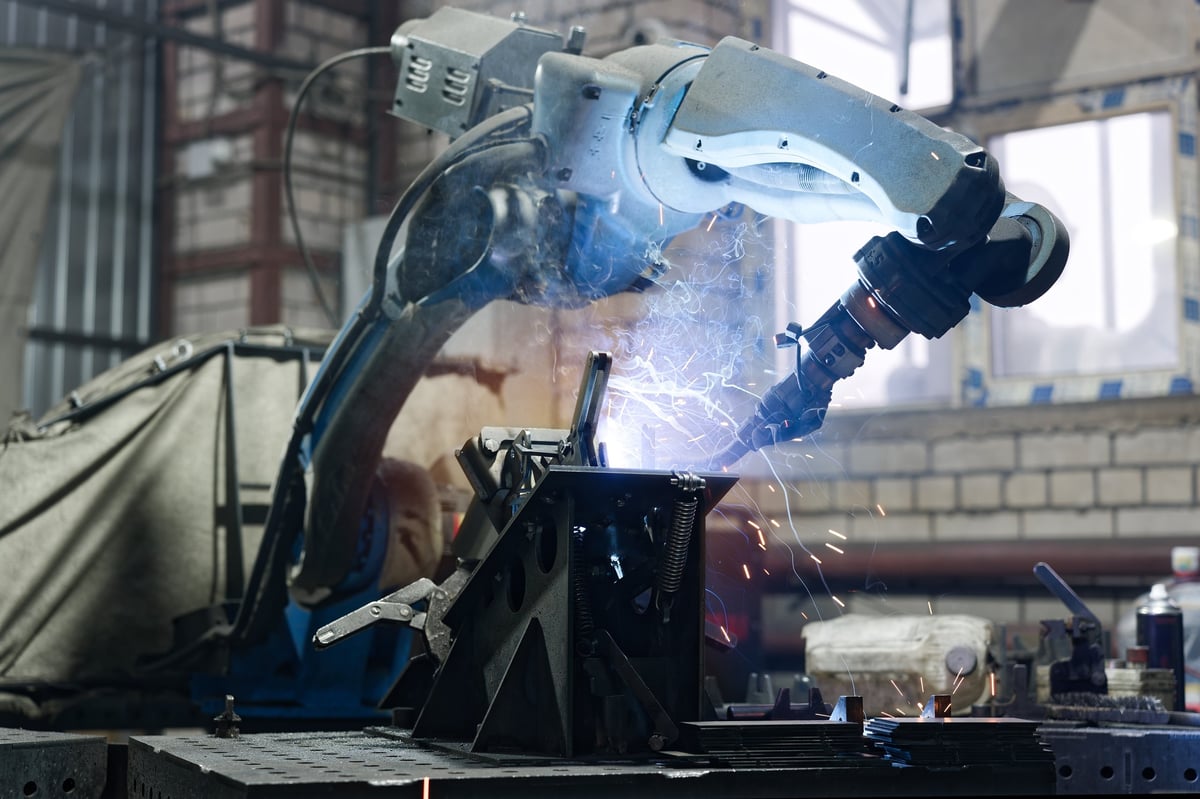 Robotic arm performing arc welding on a metal part, sparks flying in a high-tech automated production environment