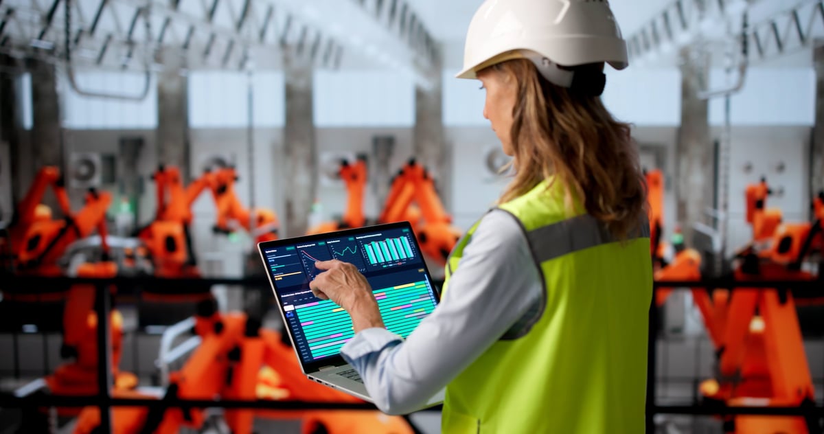 Mature woman engineer designing digital systems on a laptop in a busy factory