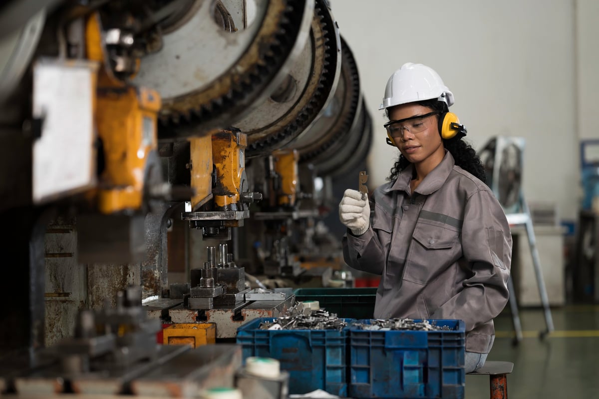 Woman industrial worker operating a metal sheet stamping press in a factory